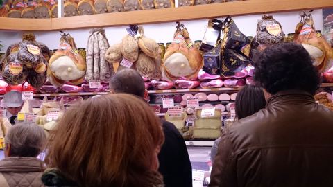 Clientes na fila da Salumeria Simoni. Vale apreciar a paisagem de salames e prosciuttos atrás do balcão